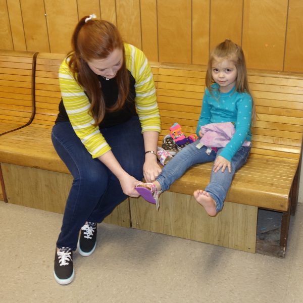 9 - A volunteer helps a little girl try on shoes